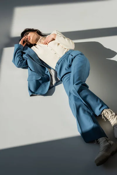 high angle view of woman in blue suit and boots lying on grey background with lighting and shadows
