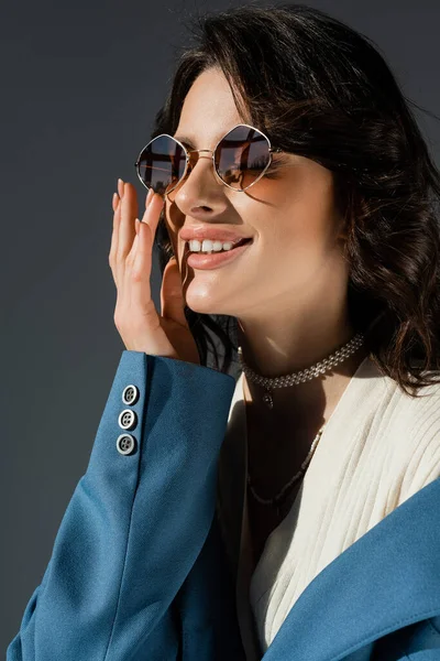 stock image portrait of smiling fashionable woman in sunglasses holding hand near face isolated on grey