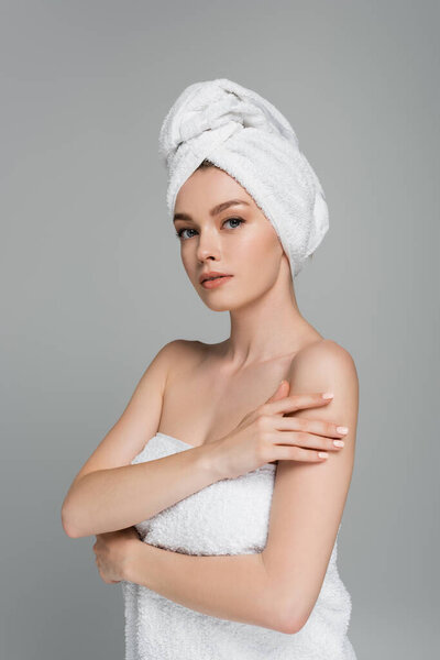 молодая женщина с голыми плечами и полотенцем на голове трогательная рука, изолированная на сером 