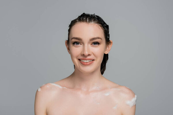 счастливая молодая женщина с мокрыми волосами и обнаженными плечами, улыбающаяся изолированно на сером 