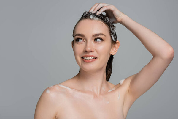 веселая молодая женщина, моющая пенные волосы, изолированные на сером
