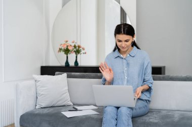 Kulaklıklı Freelancer evdeki kanepede dizüstü bilgisayarla video görüşmesi yapıyor. 