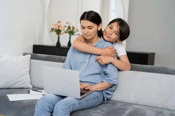 Smiling Asian Child Hugging Mom Using Laptop Living Room — Stock Photo, Image
