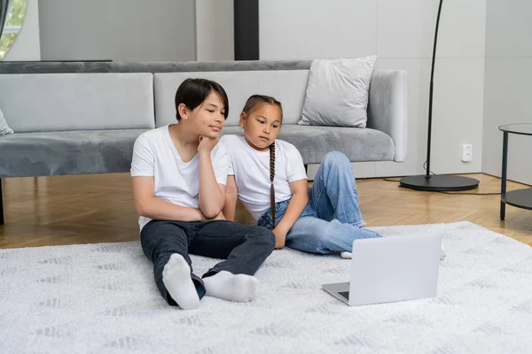 Asian siblings watching cartoons on laptop in living room