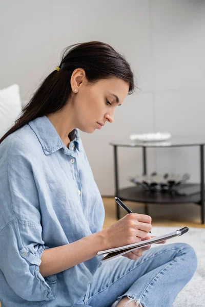 stock image Side view of woman in shirt writing on notebook at home 