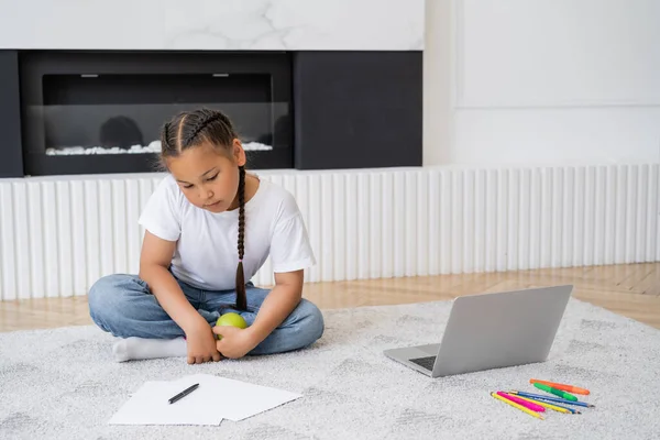 stock image Asian girl holding apple near laptop and color pencils at home 