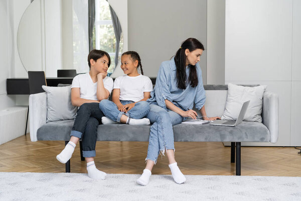 Cheerful asian kids talking while mother working on laptop at home 