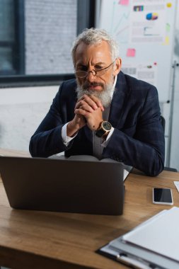 Ofiste kağıt ve akıllı telefonun yanındaki dizüstü bilgisayara bakarak odaklanmış bir iş adamı. 