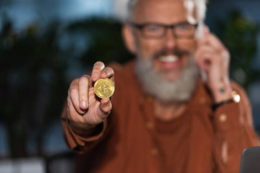 KYIV, UKRAINE - 17 Kasım 2022: Orta yaşlı mutlu iş adamının elindeki altın bitcoin 'in seçici odağı 