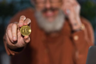 KYIV, UKRAINE - 17 Kasım 2022: Bulanık arkaplandaki olgun iş adamının elinde seçici altın ve parlak bitcoin odağı