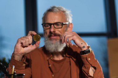 KYIV, UKRAINE - 17 Kasım 2022: Bulanık arka planda altın bitcoin tutan pozitif sakallı iş adamı