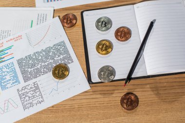 KYIV, UKRAINE - 17 Kasım 2022: Kalem yakınındaki boş defter ve ofis masasındaki belgeler üzerindeki bitcoin 'lerin üst görünümü
