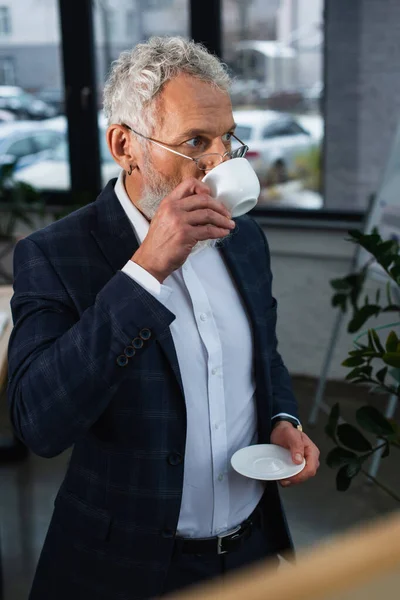 戴眼镜的灰发商人在办公室喝咖啡 — 图库照片