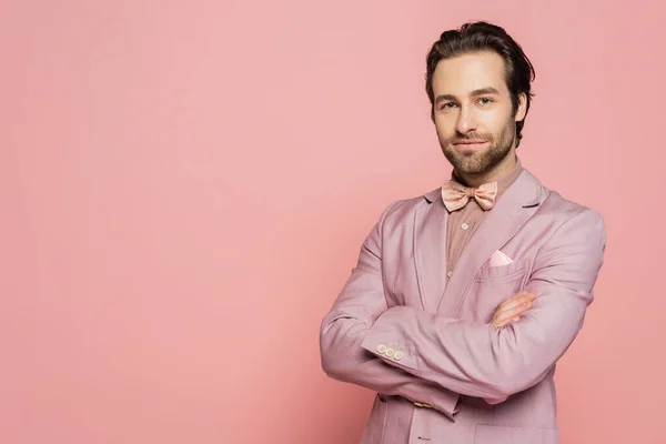 Confident host of event crossing arms and looking at camera on pink background