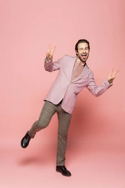 Full length of cheerful host of event showing peace sign on pink background
