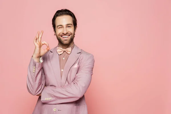 Positive host of event showing okay gesture and winking isolated on pink
