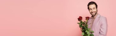 Güller tutan ve gülümseyen genç bir ev sahibi pembe pankartta izole edilmiş bir şekilde yüzünü çeviriyor. 