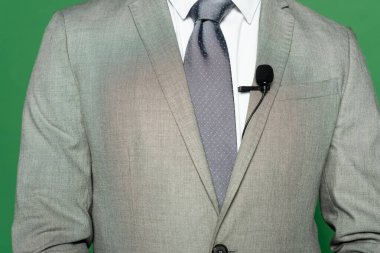 Takım elbiseli haber spikeri ve yeşilin üzerinde duran klipsli mikrofon görüntüsü 