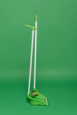 broom and plastic scoop on green background, housekeeping concept  clipart