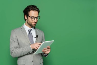 Gözlüklü ve takım elbiseli gazeteci yeşil üzerinde izole edilmiş dijital tablet kullanıyor 
