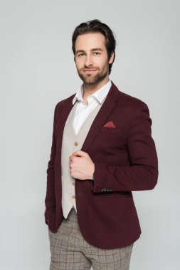 bearded showman in vest and red blazer standing with hand in pocket isolated on grey  clipart
