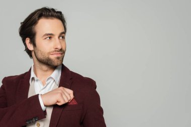 Sakallı şovmen, gri ceketin cebindeki mendili düzeltiyor.