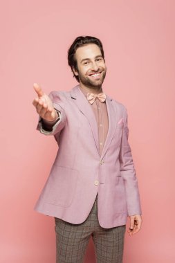 Takım elbiseli, papyonlu neşeli ve genç bir şovmen. Pembe üzerine izole edilmiş uzanmış elleri var. 