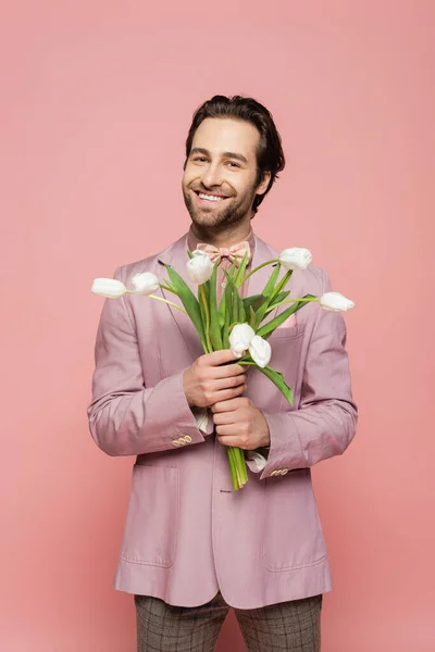 Positive host of event holding tulips and looking at camera on pink background