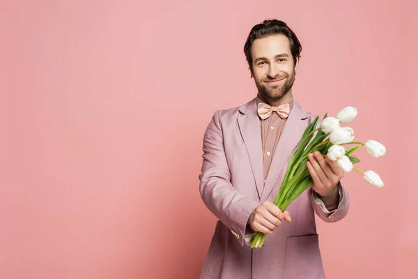 stock image Bearded host of event holding white tulips and looking at camera on pink background 