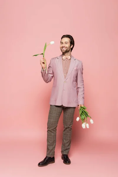 Stylish host of event holding bouquet of white tulips on pink background