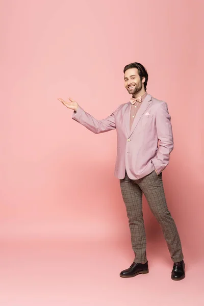 Full length of positive host of event pointing with hand on pink background