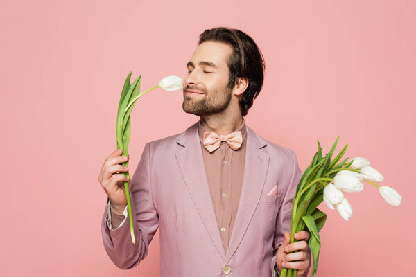 Brunette host of event in jacket smelling tulip isolated on pink 