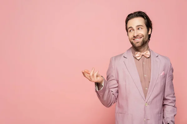 Young host of event in jacket and bow tie pointing with finger isolated on pink