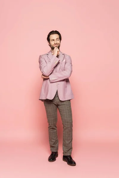 Full length of thoughtful host of event looking away on pink background