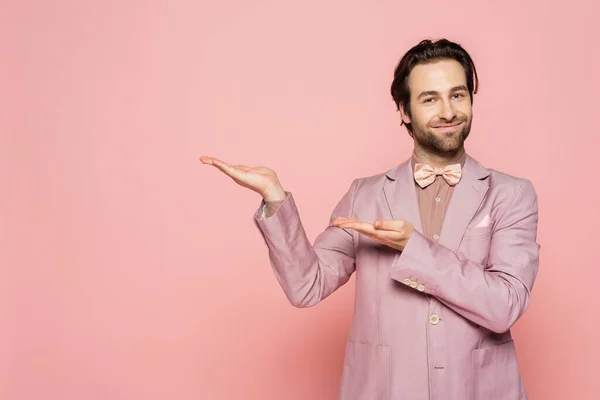 Positive host of event in jacket and bow tie pointing with hands on pink background
