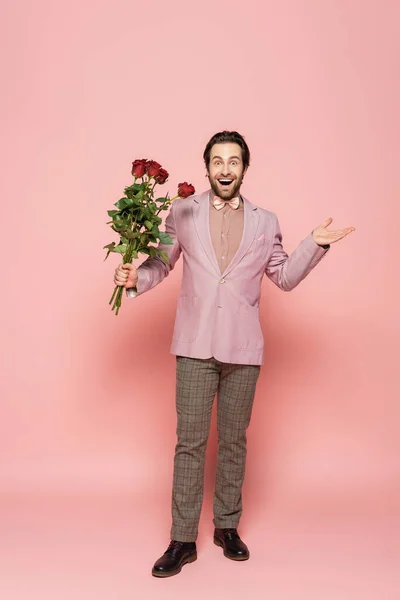 Excited host of event in jacket and bow tie holding bouquet of roses on pink background