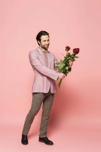 Full length of trendy host of event holding bouquet of roses on pink background