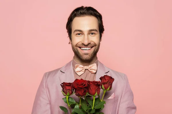 Portrait of positive host of event holding roses and looking at camera isolated on pink