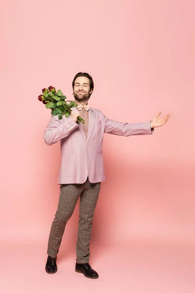 Full length of stylish host of event holding red doses and pointing with hand on pink background