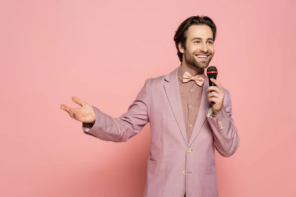 Positive host of event talking and holding microphone on pink background