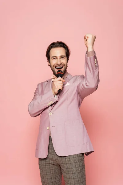 stock image Excited host of event showing yes gesture and talking at microphone on pink background 