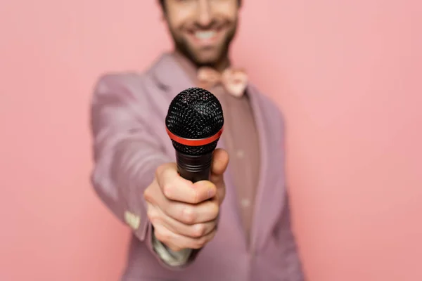 Cropped view of blurred host of event holding microphone isolated on pink