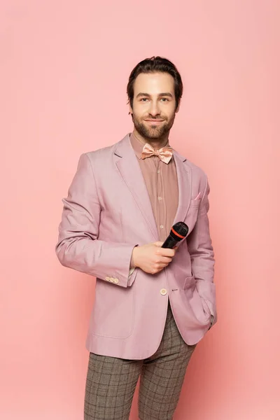 Portrait of host of event in bow tie and jacket holding microphone isolated on pink