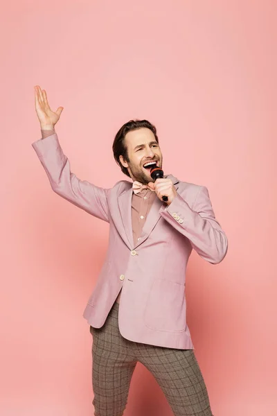 Cheerful host of event singing while holding microphone on pink background