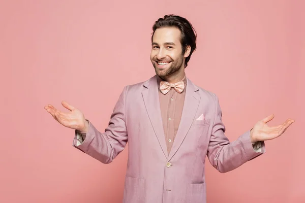stock image happy and young showman in suit with bow tie gesturing isolated on pink 