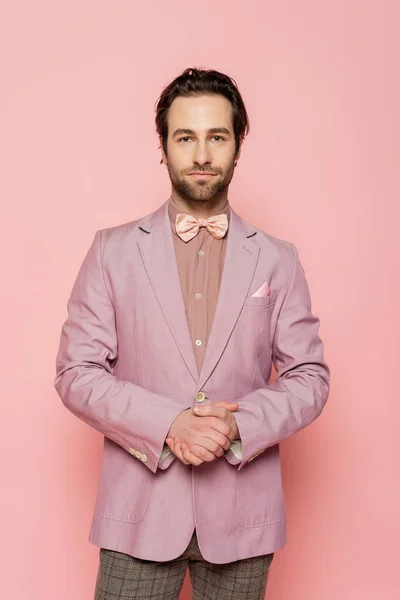 stock image bearded and young showman in suit with bow tie standing with clenched hands isolated on pink 