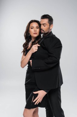 tutkulu bir adam, gri elbiseli esmer bir kadının bacağına dokunuyor. 