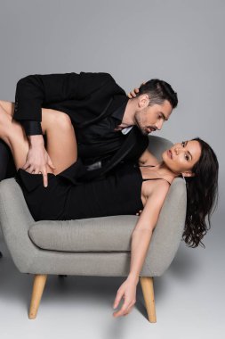 Sakallı adam kumral kadını baştan çıkarıyor. Gri koltukta yatıyor. 