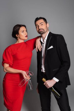 Kırmızı elbiseli, gözlüklü ve gri arka planda şampanya içen seksi bir kadın. 