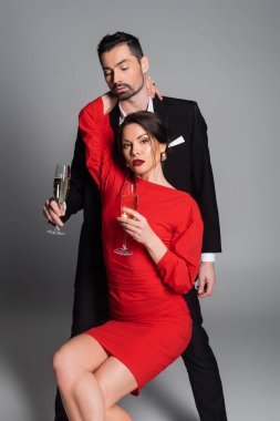 Elbiseli seksi kadın, erkek arkadaşına sarılıyor ve gri arka planda şampanya tutuyor. 